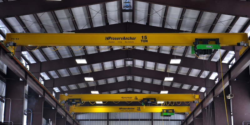 Multiple 15-ton yellow overhead cranes installed inside the Woven Metal Products manufacturing facility.